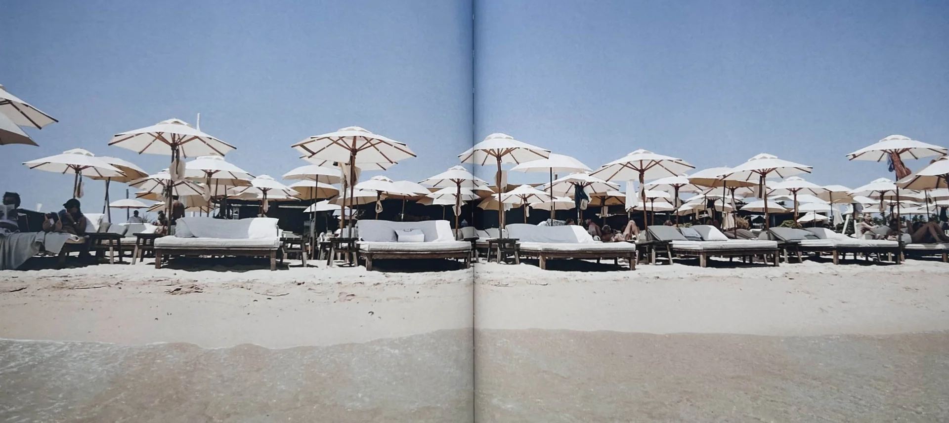 Open spread of French Summer showing white beach umbrellas and loungers on the sand